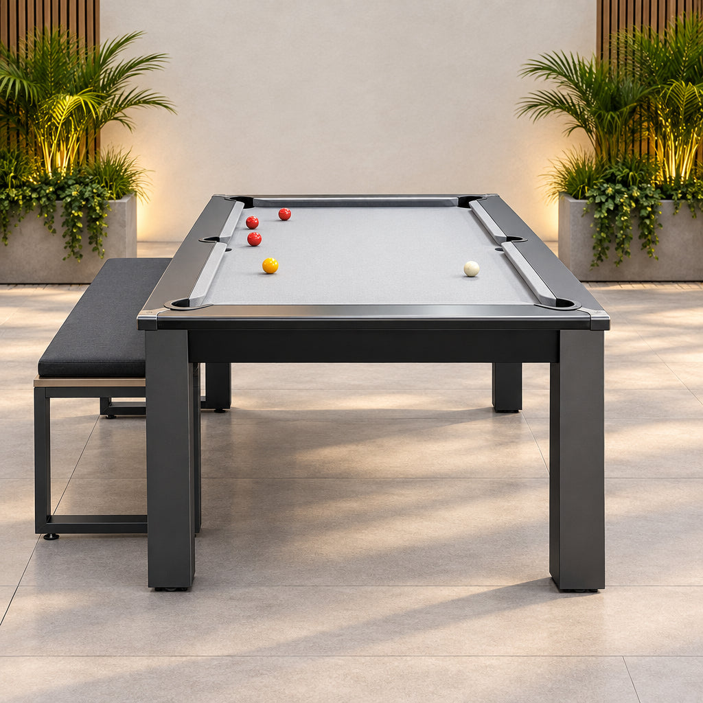 A rectangular pool dining table with a gray felt surface, dark gray metal frame, and matching bench, shown in an indoor room with blue carpet and a wood-paneled wall.