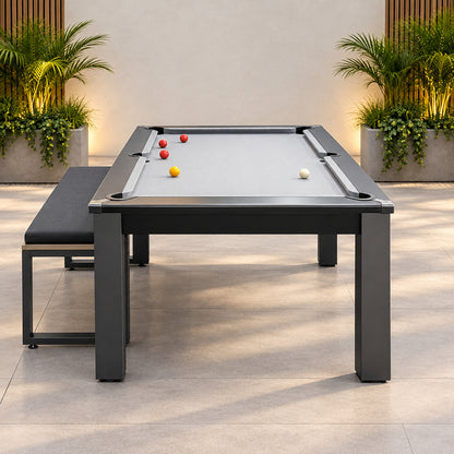 A rectangular pool dining table with a gray felt surface, dark gray metal frame, and matching bench, shown in an indoor room with blue carpet and a wood-paneled wall.