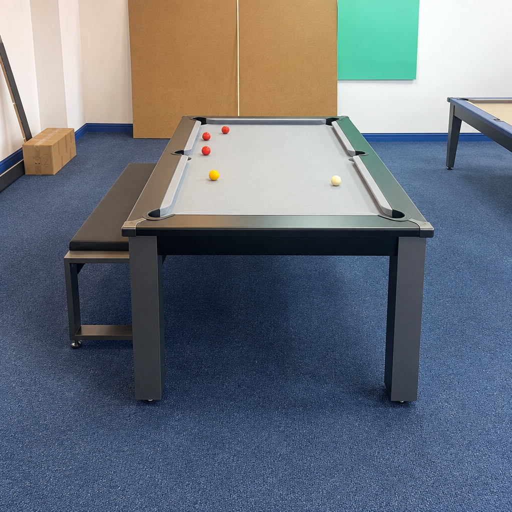 A rectangular pool dining table with a gray cloth surface, dark gray metal frame, and matching bench, shown in an indoor room with blue carpet.